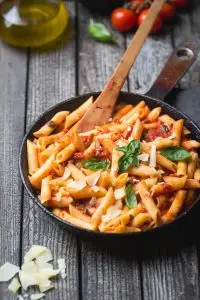 Penne pasta in tomato sauce and cheese decorated with basil on a wooden background