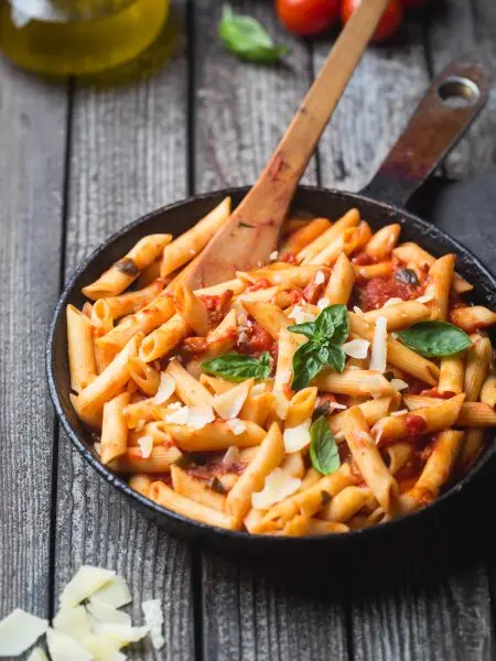 Penne pasta in tomato sauce and cheese decorated with basil on a wooden background