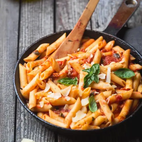 Penne pasta in tomato sauce and cheese decorated with basil on a wooden background