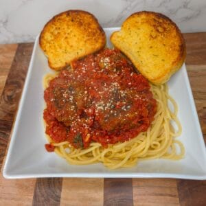 Crispy garlic bread slices with spaghetti and meatball marinara on white plate.