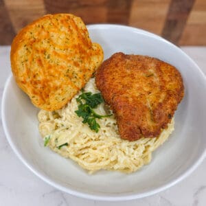 Crispy fried chicken with creamy mashed potatoes and garlic bread on white plate.