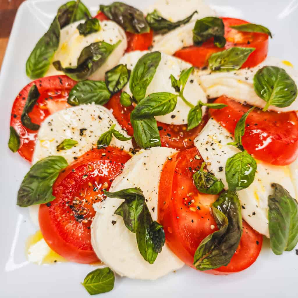 Fresh Caprese salad with ripe tomatoes, fresh mozzarella, basil leaves, and black pepper.