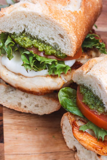 A sandwich with tomatoes and cheese on a wooden cutting board.