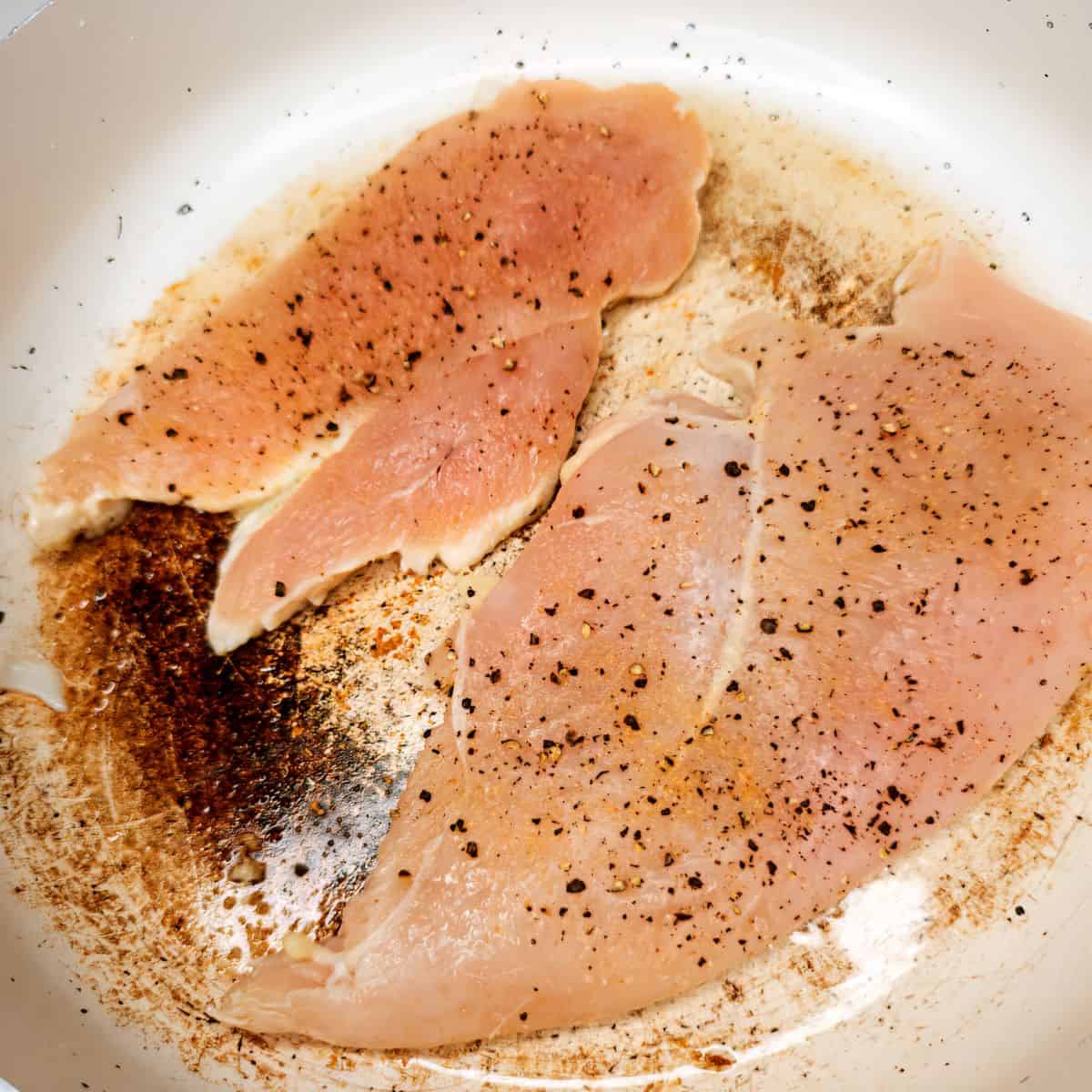 Seasoned raw chicken breasts cooking in a skillet for Italian recipes.