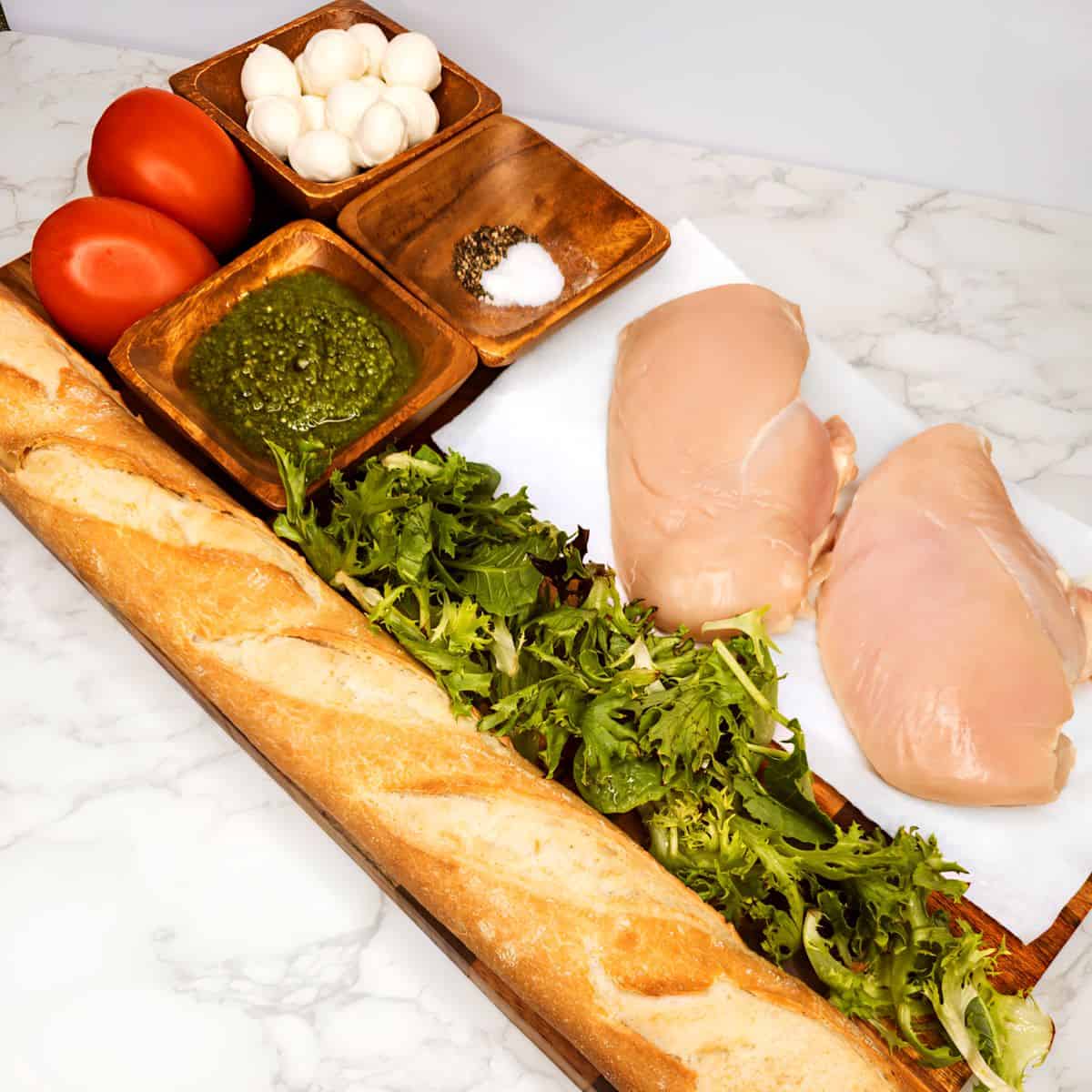 Fresh Italian chicken sandwich ingredients with bread, chicken breast, tomatoes, basil, mozzarella, and seasonings for authentic Italian cooking ideas.