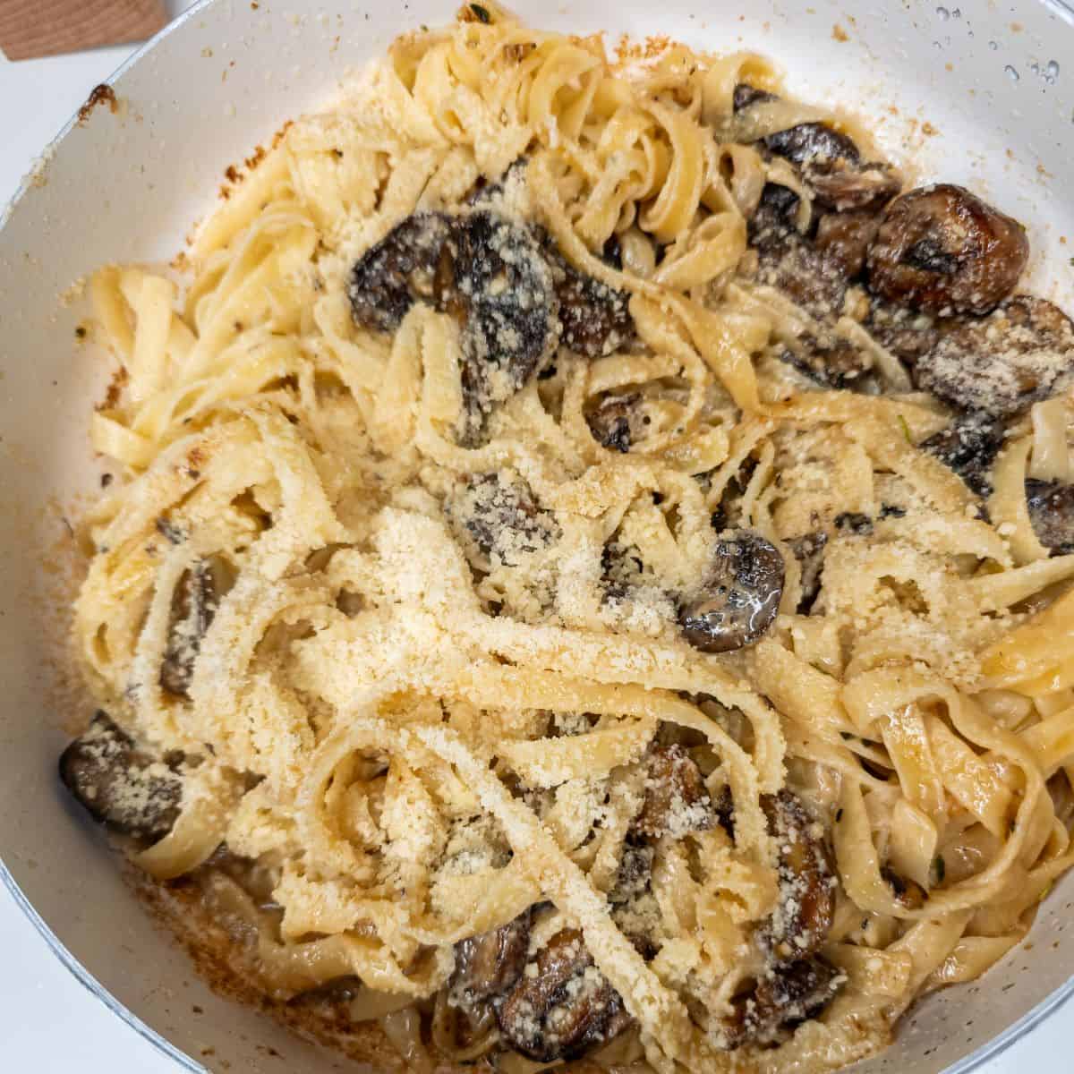 Crispy mushroom fettuccine with parmesan cheese in a white skillet.