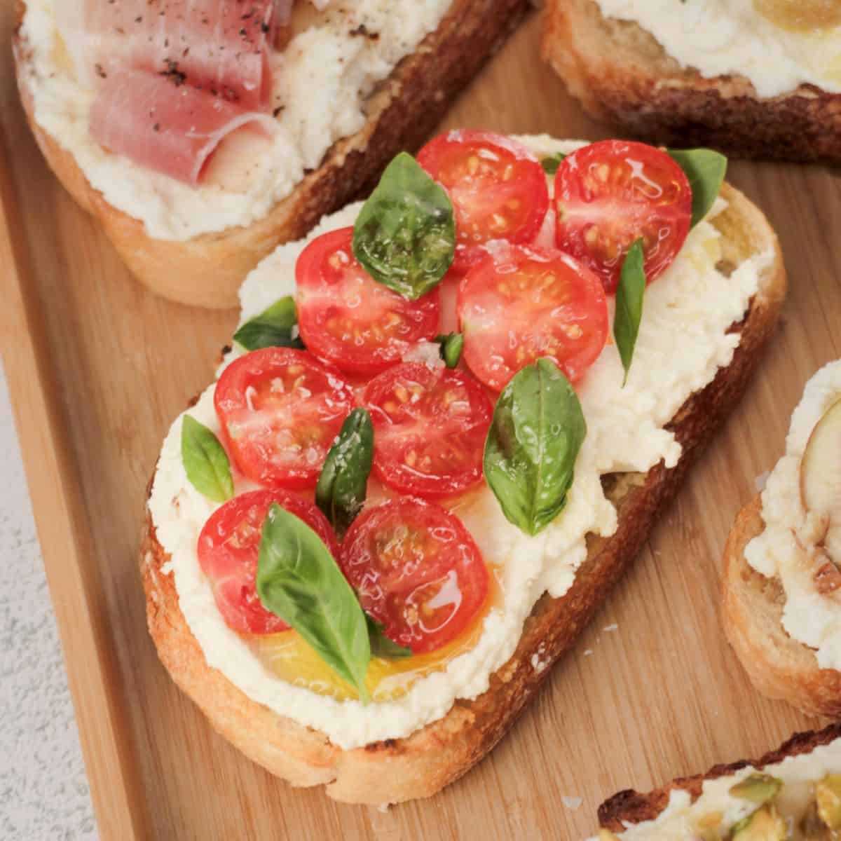 Fresh cherry tomatoes and basil leaves on creamy cheese spread over crusty bread slice.