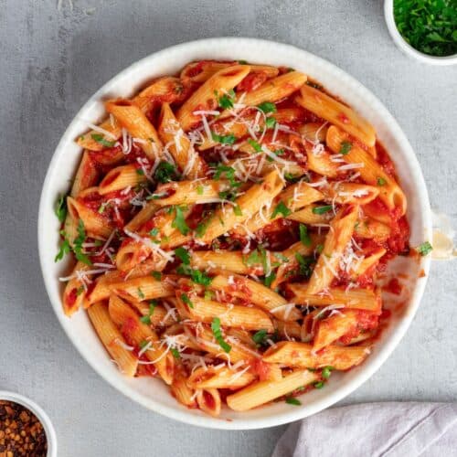 Delicious Italian pasta penne allarrabbiata served with rich tomato sauce, topped with grated cheese and fresh herbs.