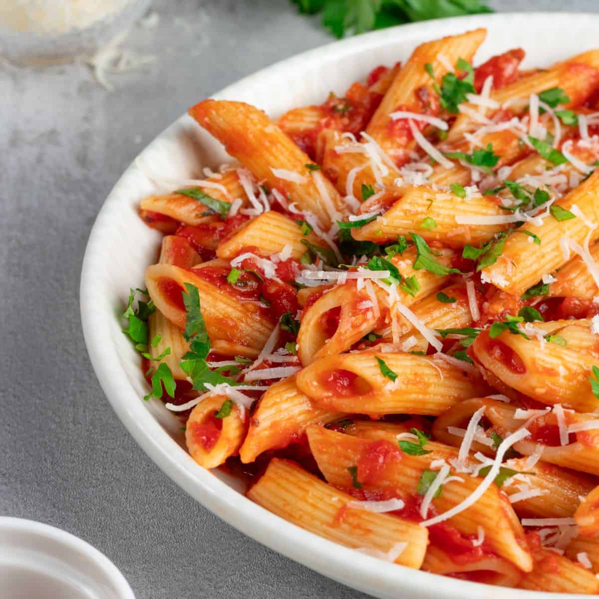 Delicious penne all arrabbiata recipe with fresh tomato sauce, garnished with grated cheese and chopped parsley.