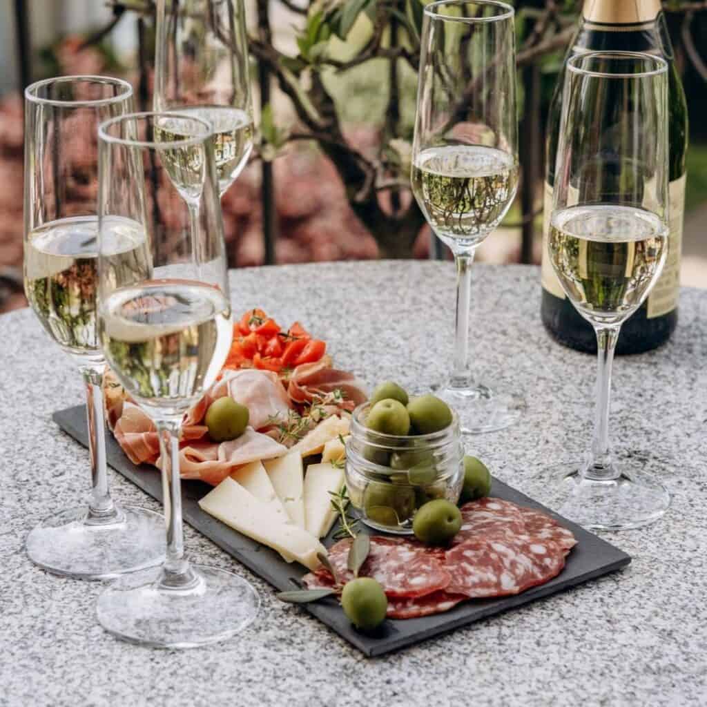 Glasses of Italian sparkling wine with cheese, olives, and cured meats on a slate platter served aperitivo.