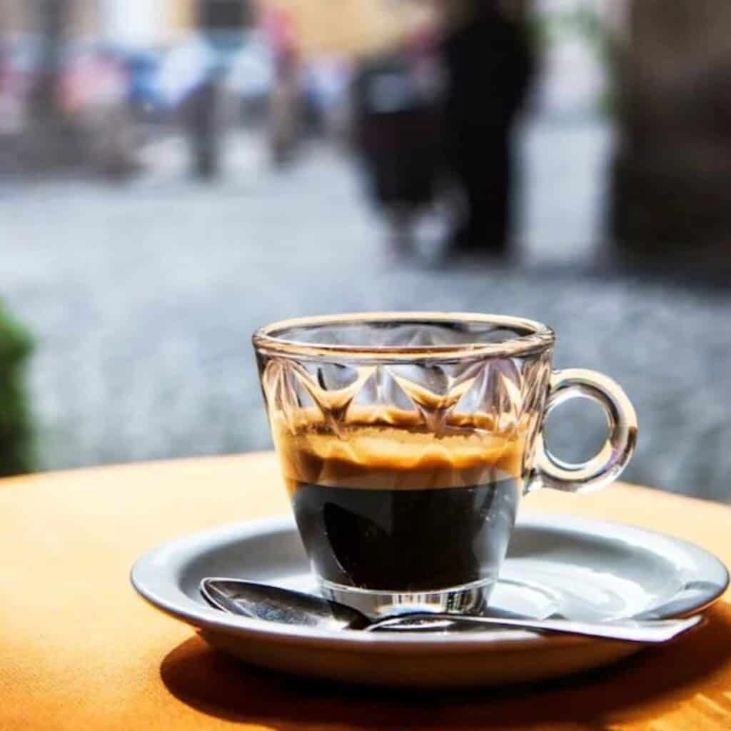 Freshly brewed caffe Italian espresso coffee in a glass cup on a wooden table.