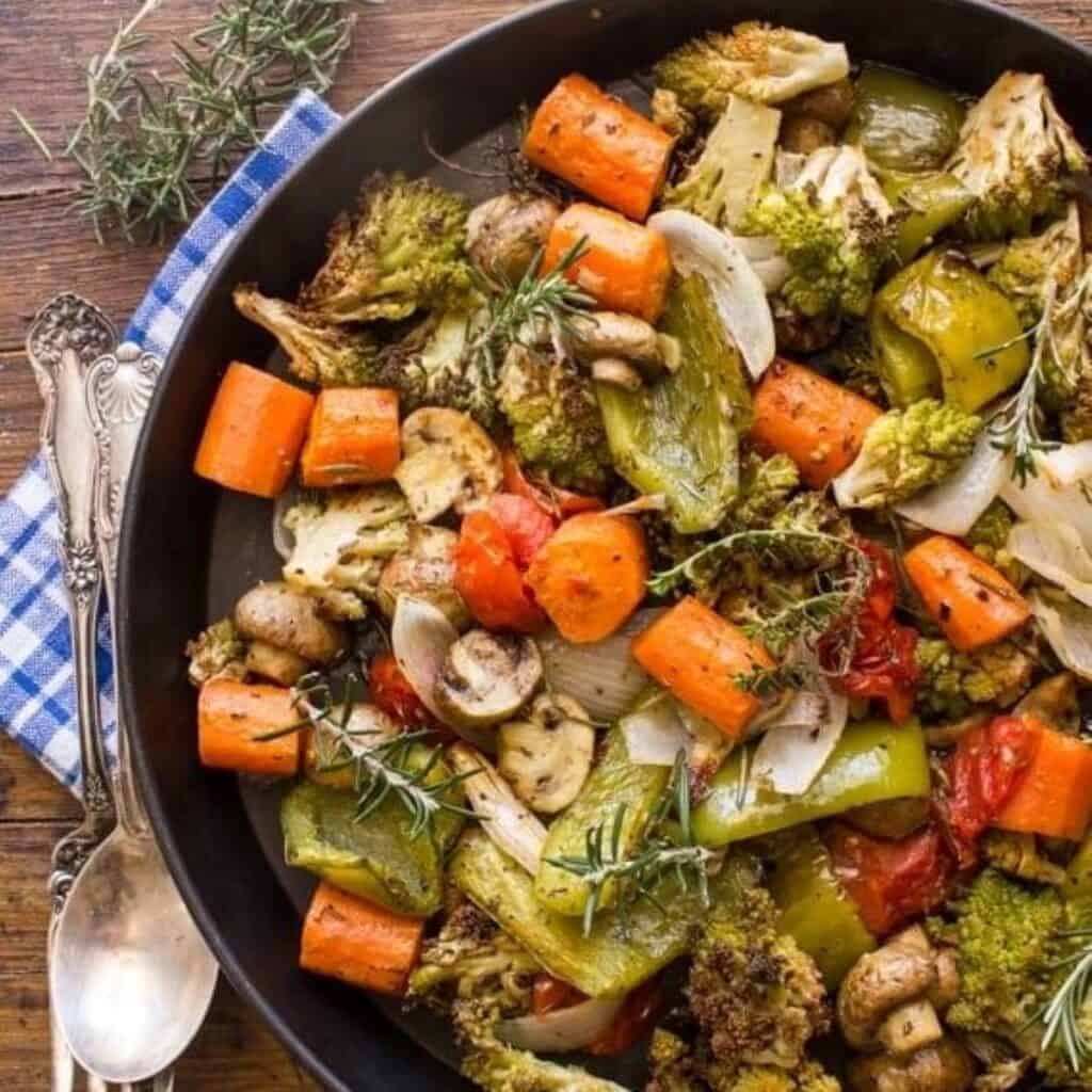 Colorful roasted Italian contorno vegetables including carrots, broccoli, mushrooms, and peppers in a skillet.
