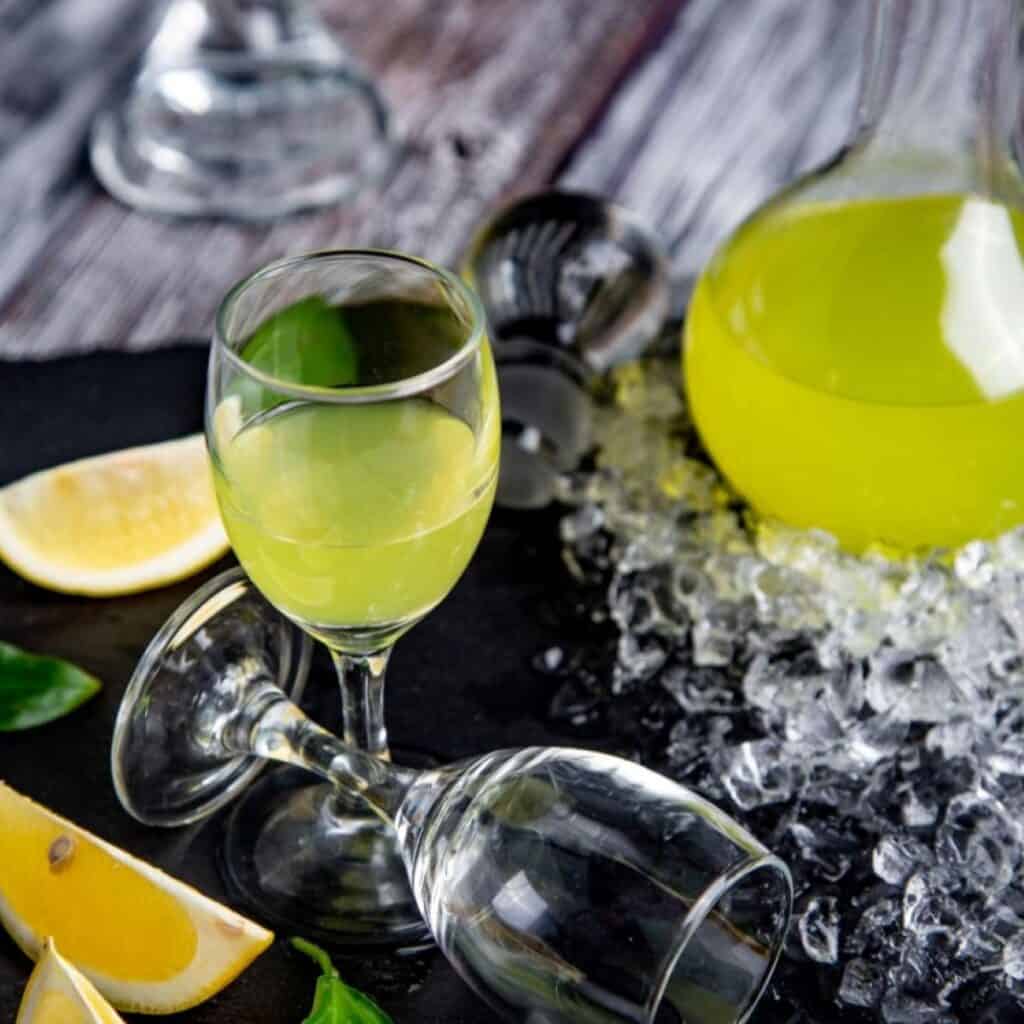 Glass of homemade Digestivo limoncello with lemon slices and ice on rustic table.